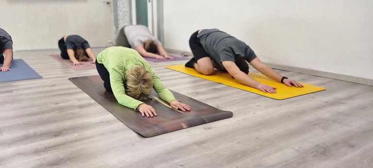 Fünf Yogateilnehmer in der Child’s Pose – Balasana welche im hellen Yogastudio von Yoga Jasmin Die Yogaübung praktizieren.